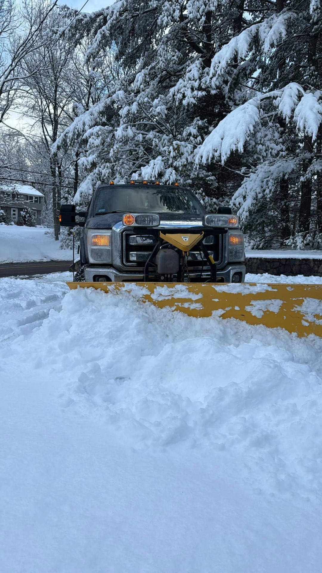 Plow truck clearing a residential driveway after a New England snowstorm